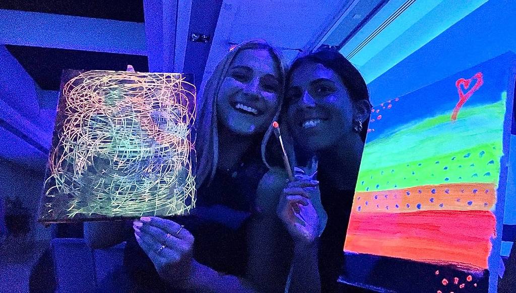 Two women holding up their neon paintings at a Neon Brush workshop