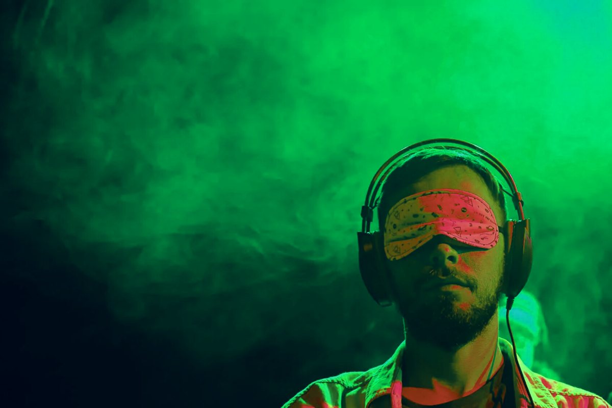 Hombre con los ojos vendados y auriculares en una atmósfera verde, participando en un concierto a oscuras diseñado para estimular los sentidos