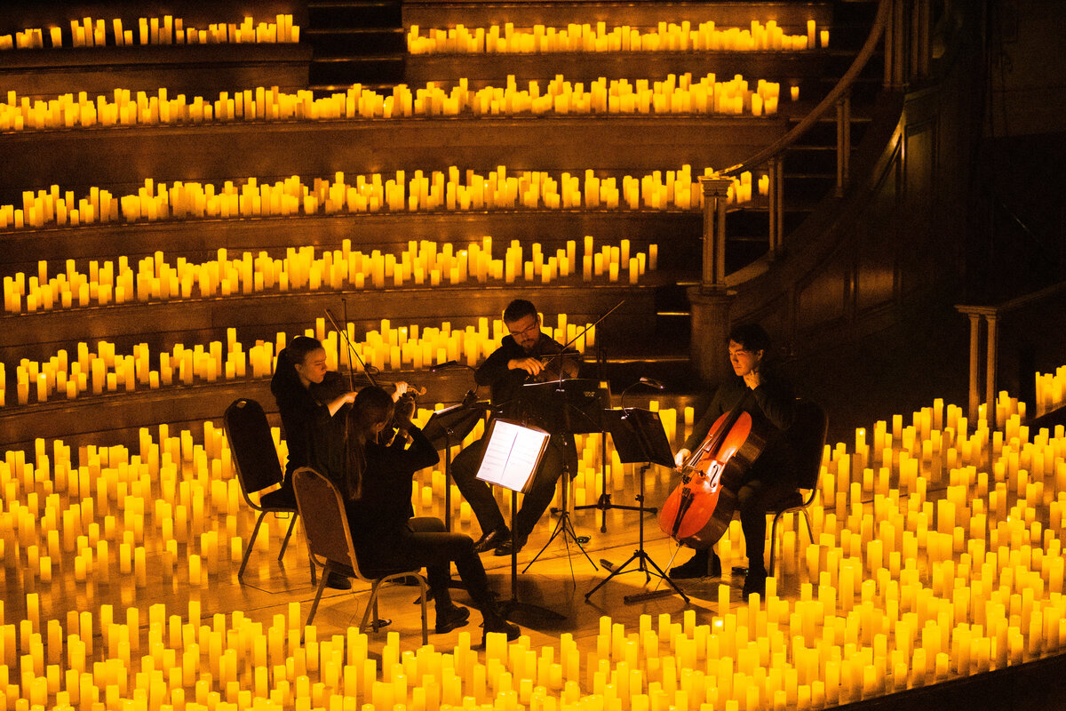 Un cuarteto de cuerda toca sobre un escenario cubierto de velas durante un concierto Candlelight.