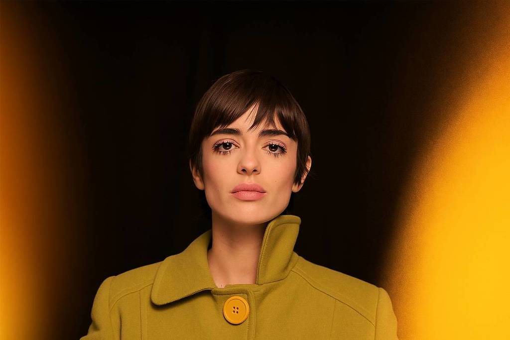 Zoe Gotusso in a green coat in front of a black background illuminated only with Candlelight candles.