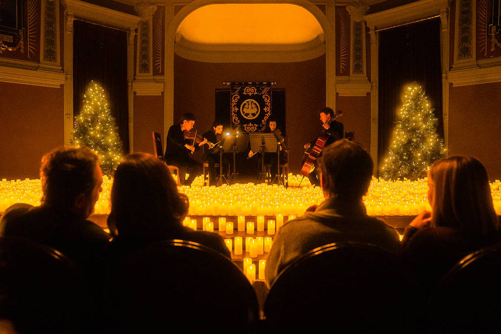 Audience enjoying a Candlelight Christmas concert, with a string quartet playing among thousands of lighted candles and trees decorated with lights.