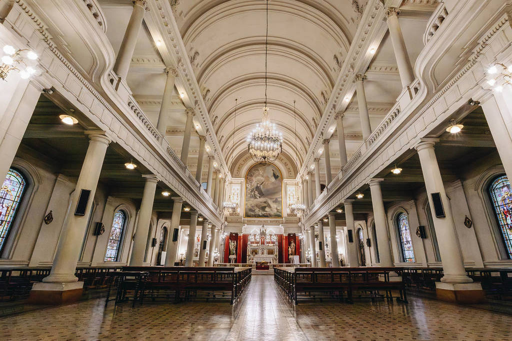 Interior de la Capilla Mayor del Colegio La Salle en Buenos Aires, con columnas blancas, vitrales y un altar iluminado al fondo.