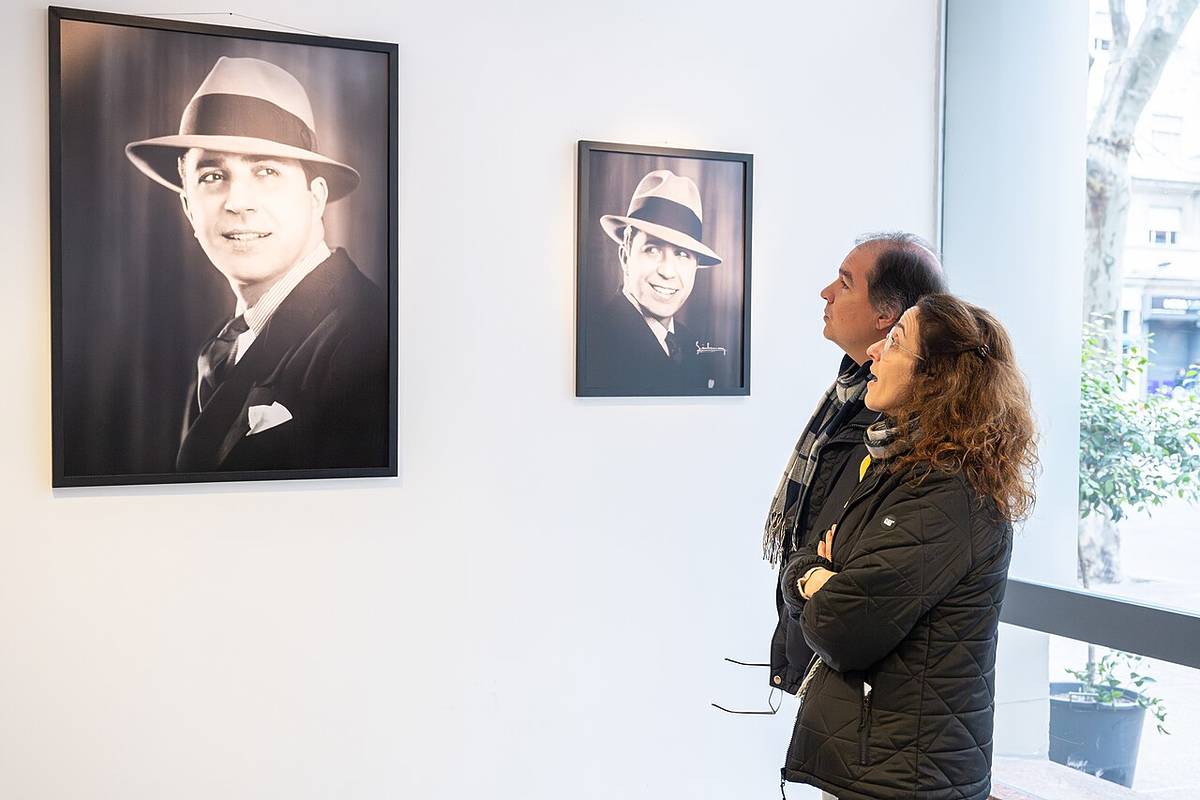 Dos visitantes observan retratos en blanco y negro de Carlos Gardel