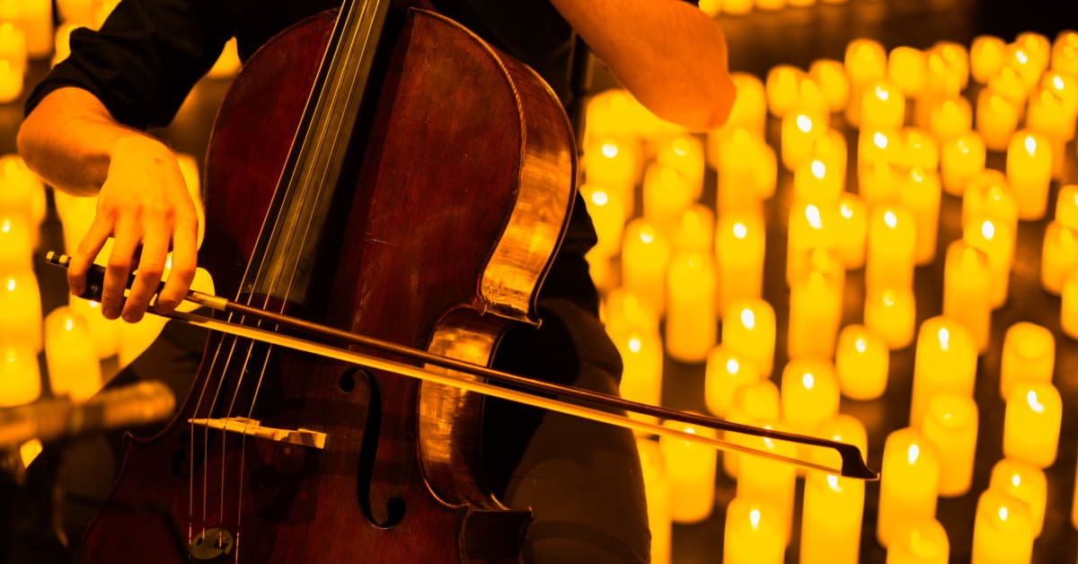 Primer plano de un músico tocando el violonchelo sobre un escenario cubierto de miles de velas en el Teatro Margarita Xirgu durante un concierto Candlelight en Buenos Aires.