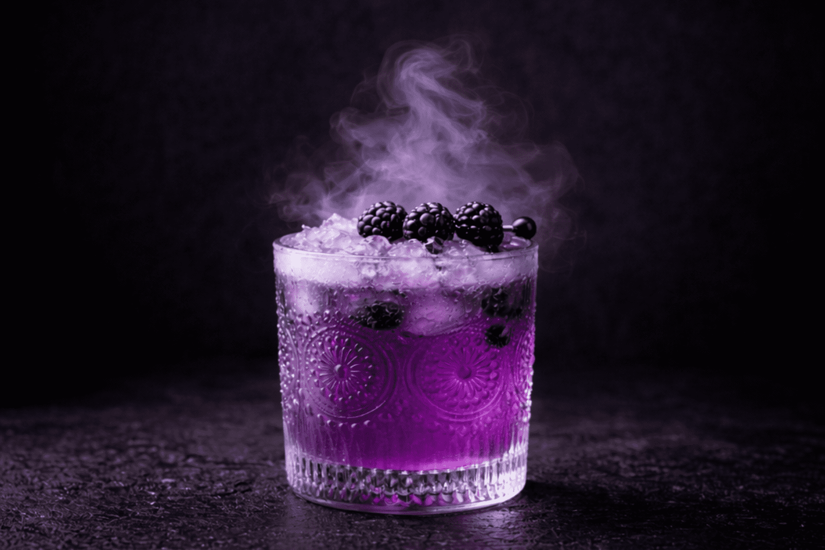Cóctel violeta con hielo, moras y humo alrededor.
