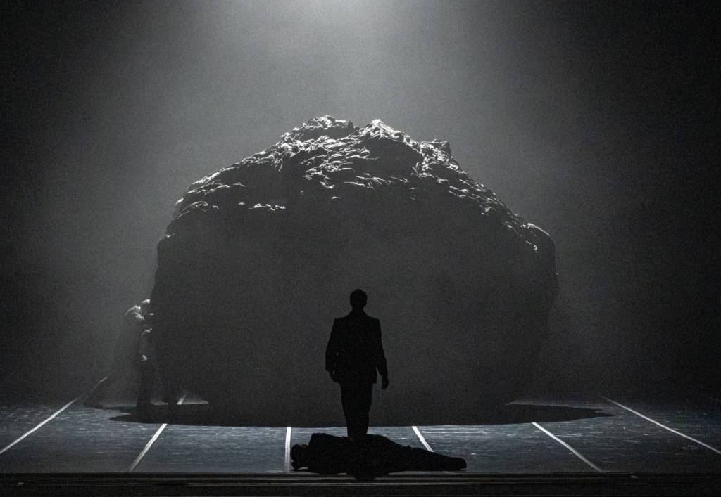 Silueta de un bailarín en contraluz frente a una gran estructura en forma de roca en el escenario del Teatro Colón durante el ballet «Principio de éxtasis»