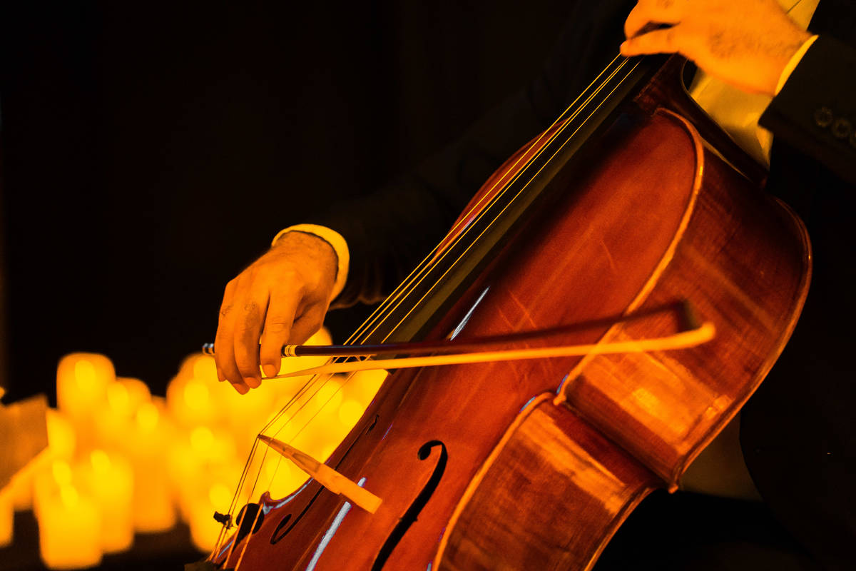 Primer plano de las manos de un músico tocando el violonchelo sobre un escenairo cubierto de miles de velas durante un concierto Candlelight.