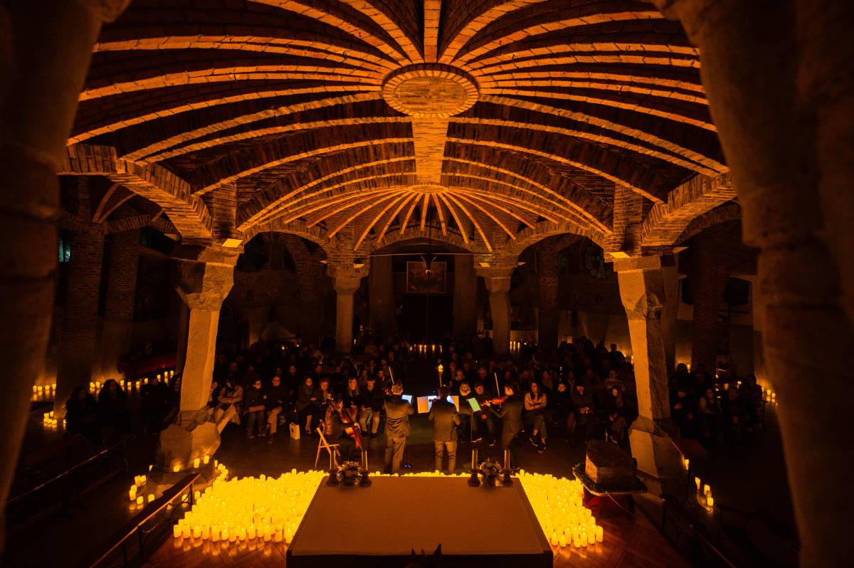 Un cuarteto de cuerda toca sobre un escenario cubierto de velas durante un concierto Candlelight en la Cripta Gaudí de Barcelona.