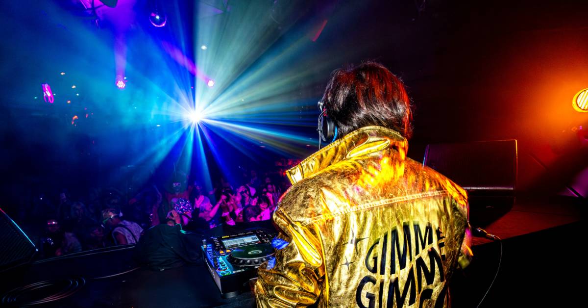 Vista desde atrás del DJ de Gimme Gimme Disco pinchando durante la fiesta frente a mucho público.