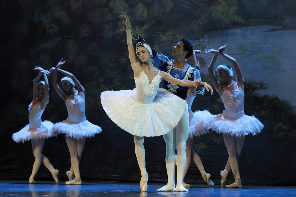 Pareja de bailarines  en una pose romántica del Lago de los Cisnes, acompañados por un conjunto de bailarinas con tutús blancos sobre un escenario teatral de ballet en Barcelona