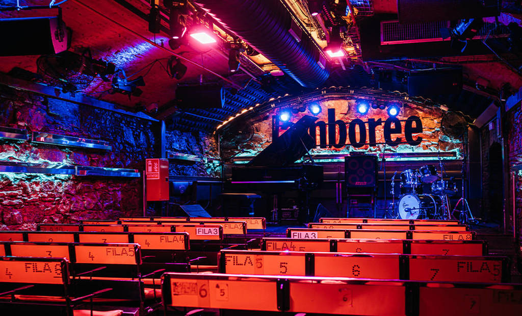 Il palco del Jamboree Barcelona illuminato con luci colorate, con pianoforte, batteria e file di sedie prima di un concerto jazz.