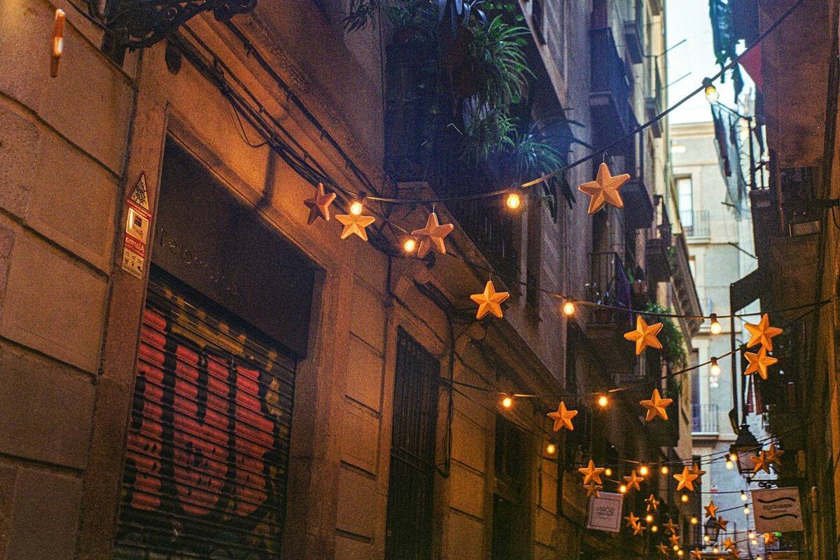 Luces navideñas en forma de estrellas iluminando una calle estrecha del Gòtic de Barcelona al anochecer