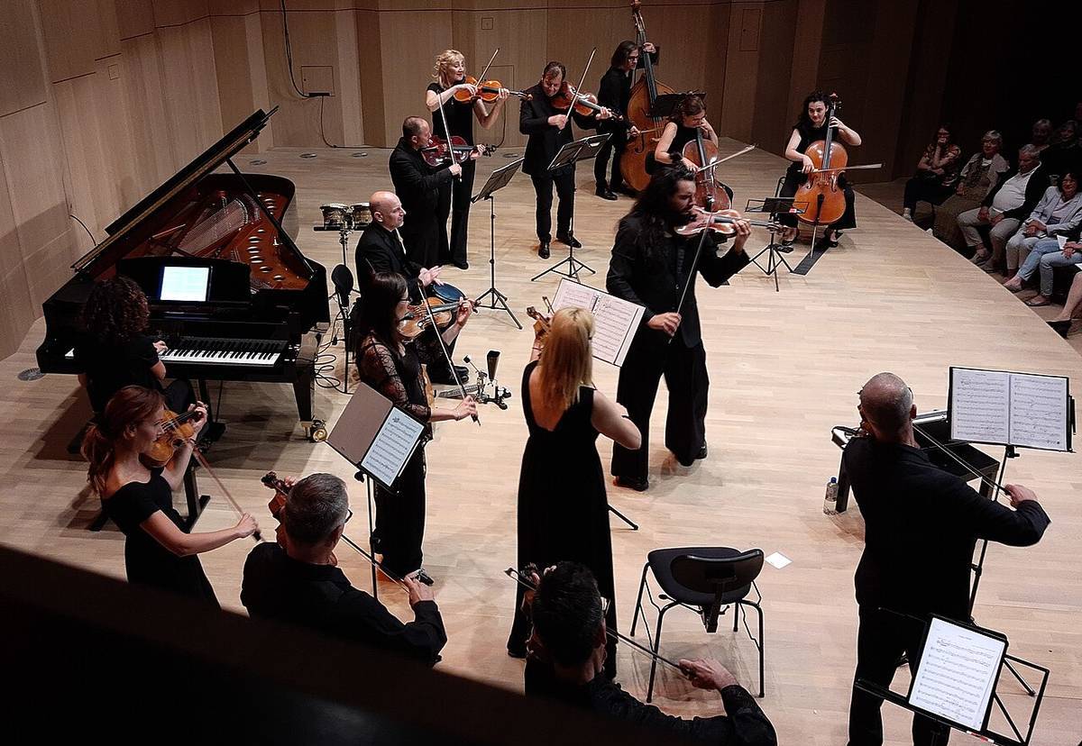 Grupo de músicos interpretando música de cámara en una pequeña sala de conciertos, con violines, violonchelos y piano sobre el escenario