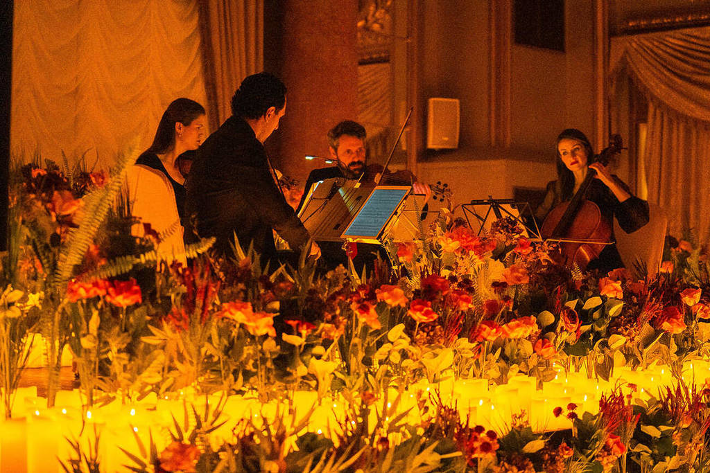 Un cuarteto de cuerda toca sobre un escenario cubierto de flores y velas en un concierto Candlelight Spring en Barcelona.