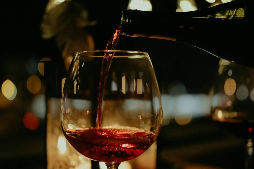 Primer plano de una botella de vino tinto llenando una copa en un bar.