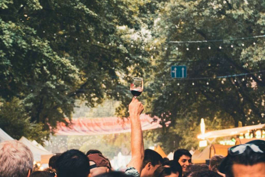 A raised hand holds a glass of red wine above a crowd at a festival