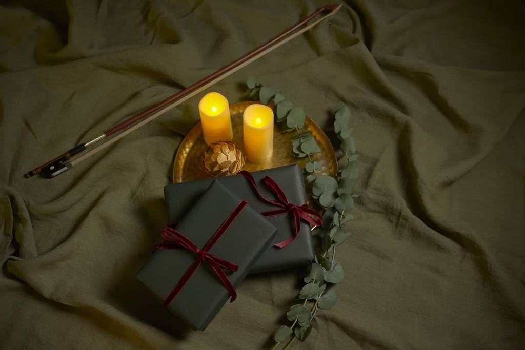 Photo of candles with a pine cone, foliage, fiddle archers and two wrapped gift packages