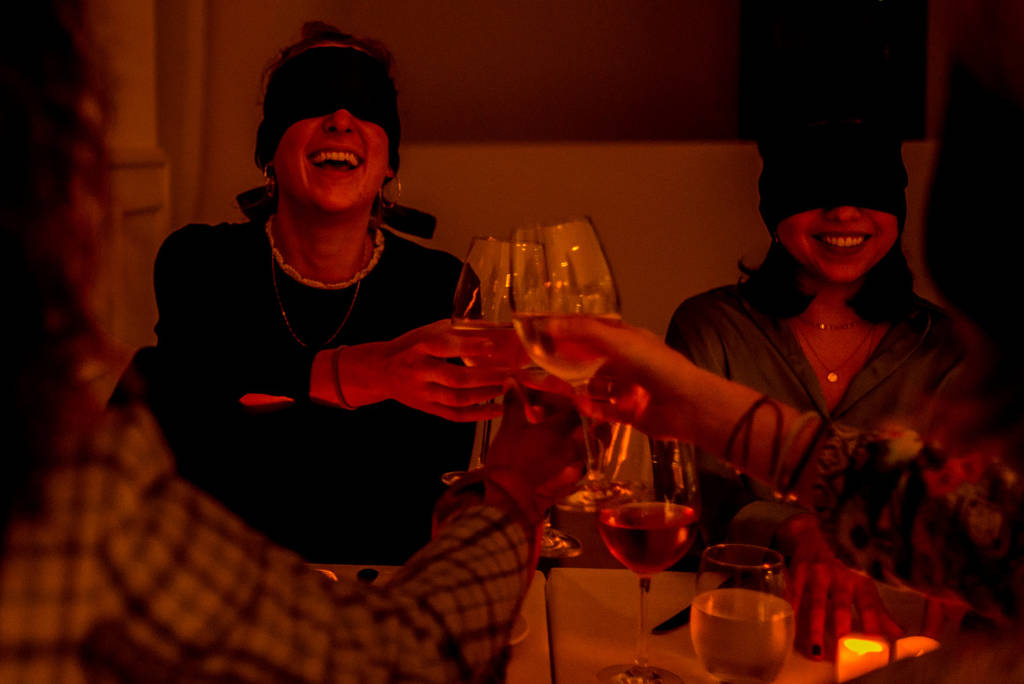 Blindfolded friends clinking glasses and laughing at Dining in the Dark