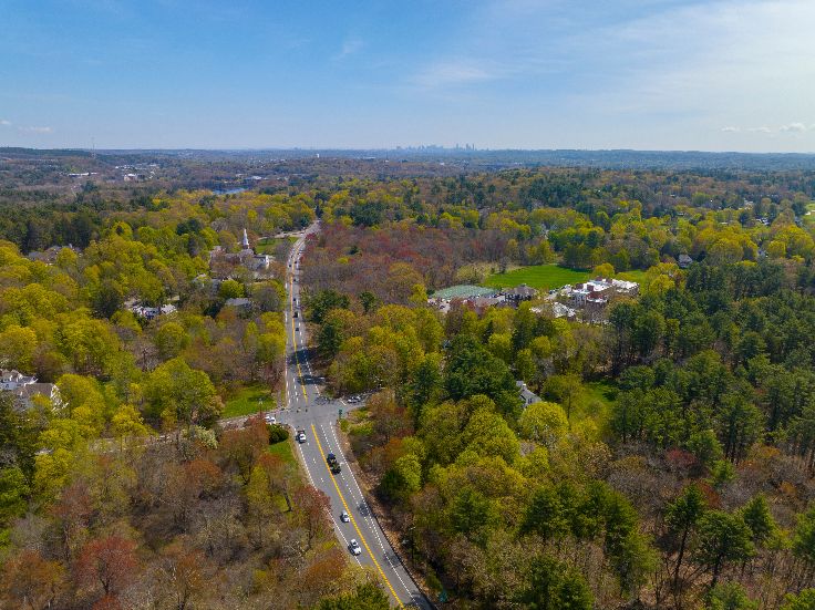 Boston Post Road on US Highway 20 aerial view with Boston Modern city skyline at the background in historic town center of Weston, Massachusetts MA, USA.