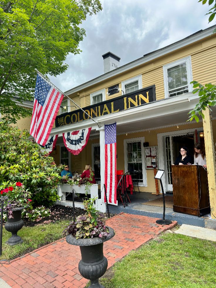 Concord, Massachusetts, USA - June 19, 2023: Exterior of Concord's Colonial Inn with people eating on the porch. Red brick path leading up to the front entrance of local business.