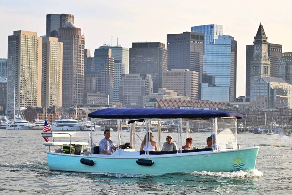 electric boat in front of boston skyline with people on boat