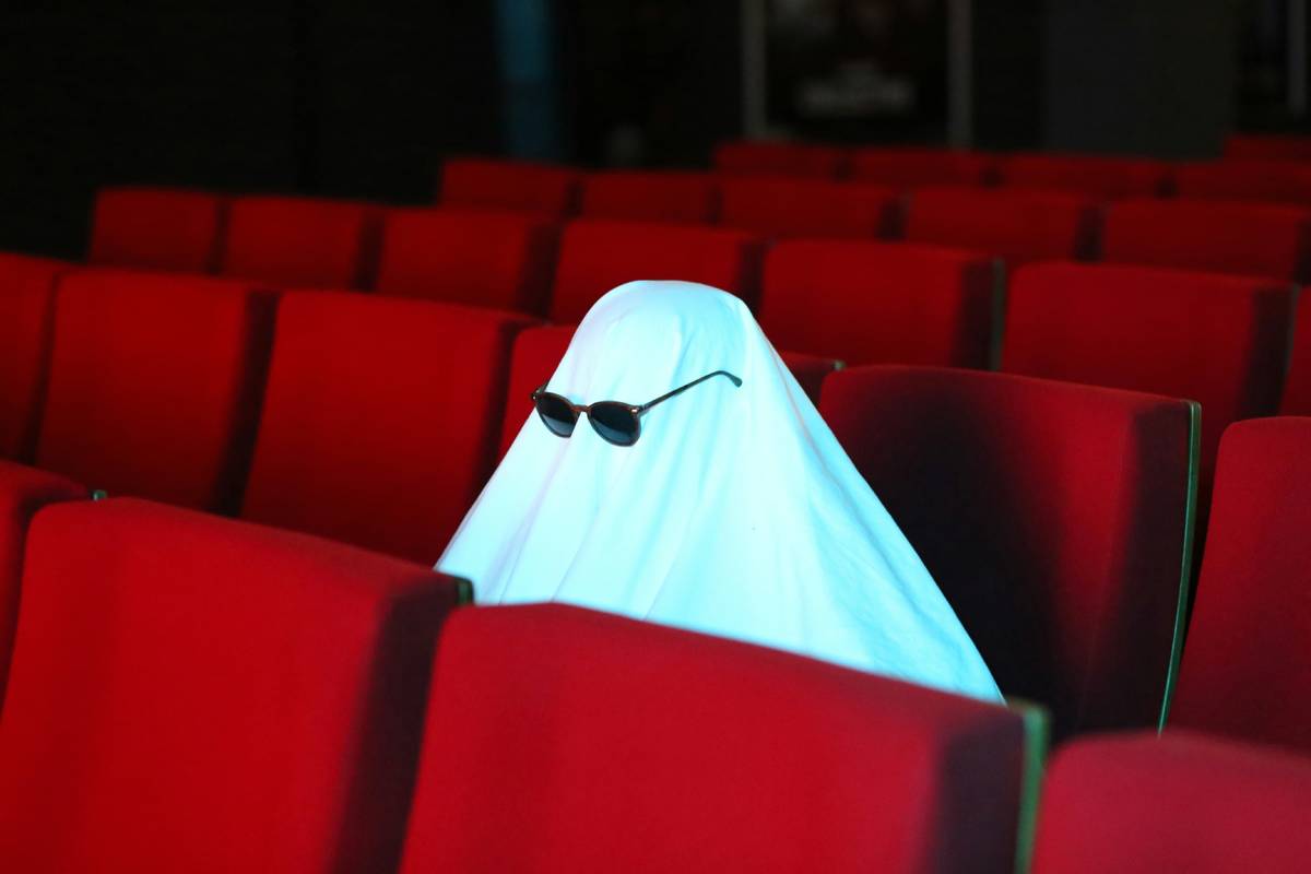 Photo d'un drôle de fantome avec des lunettes de soleil, assis tout seul dans un cinéma