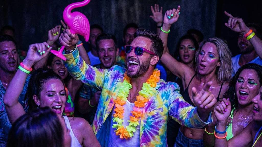 Photo d'une foule lors d'une fête avec au milieu un homme tenant un flamant rose gonflable