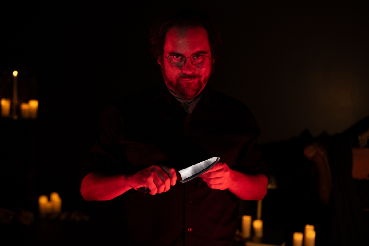 Plano medio de un actor de Serial Killer Speakeasy mirando a cámara mientras tiene un cuchillo en las manos.