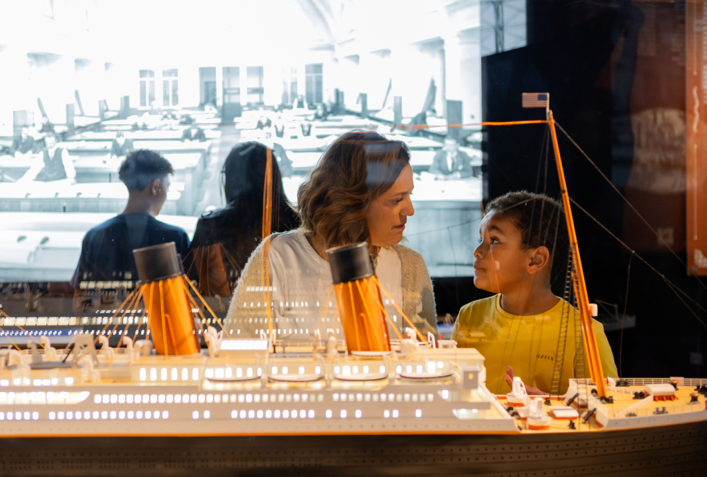 A woman and a child in front of a model of the cruise ship at “Titanic: An Immersive Voyage”