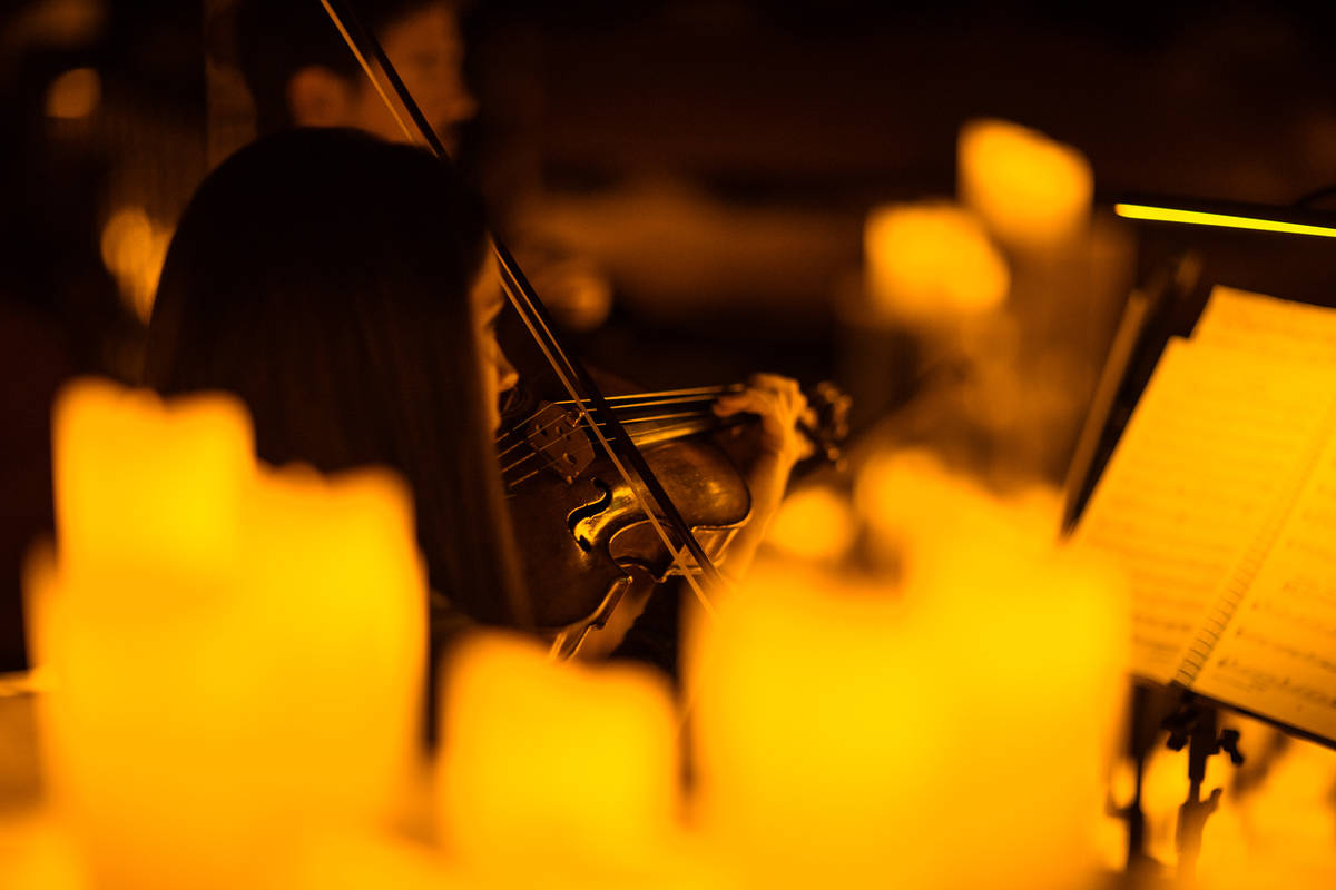Violinista rodeada de velas mientras toca y mira las partituras