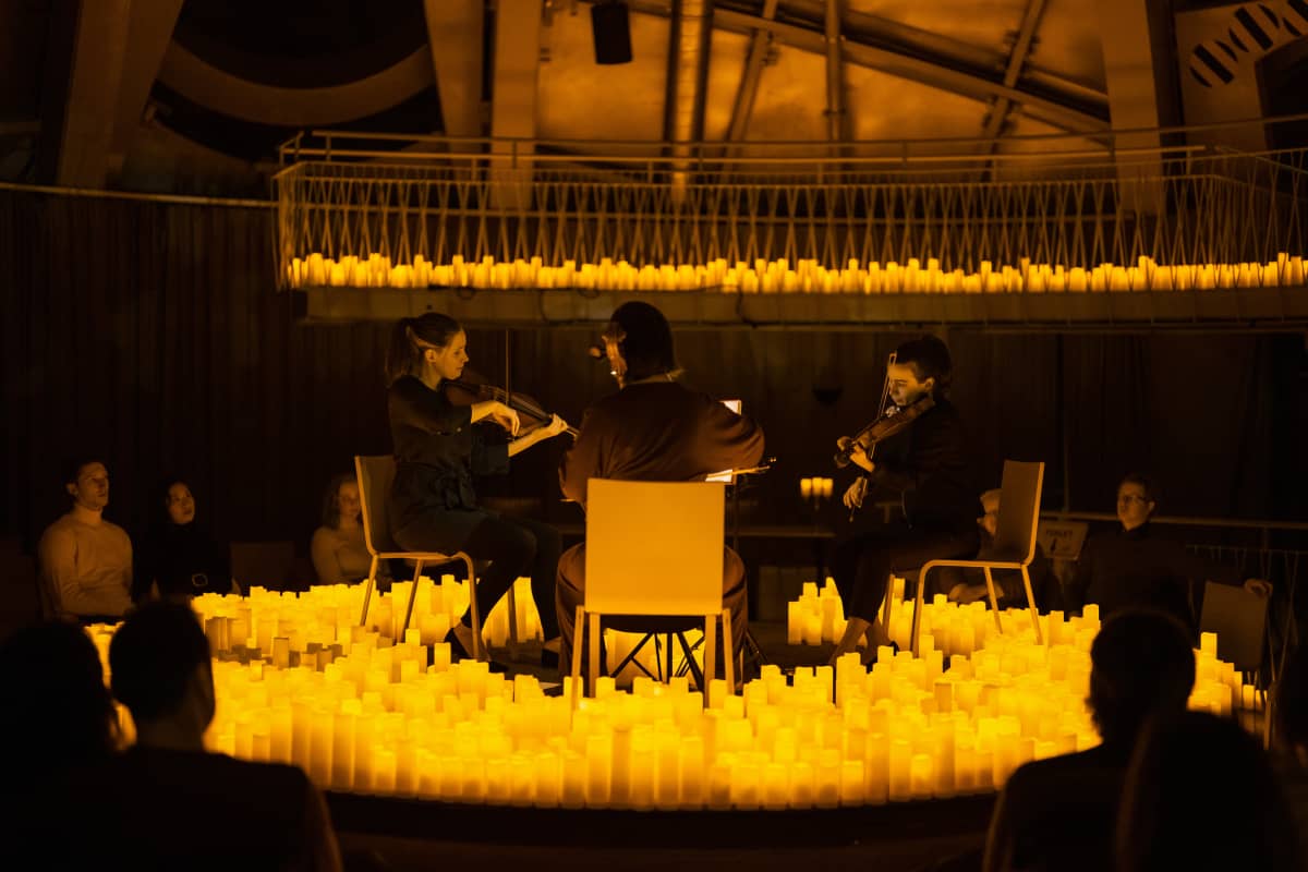 Cuarteto de cuerdas tocando en un escenario circular rodeado de velas, con el público sentado alrededor en un ambiente íntimo y cálido.