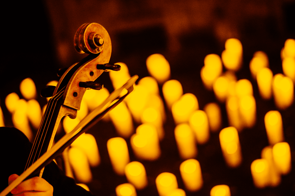 Close up of the top of a violin with the blurry glow of candles in the background.