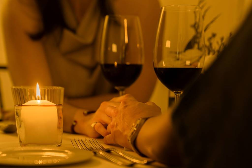 Two people hold hands over glasses of wine at Dining in the Dark.