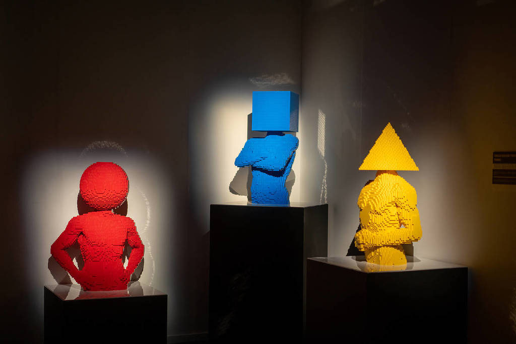 three sculptures of humans with shapes for heads in primary colours