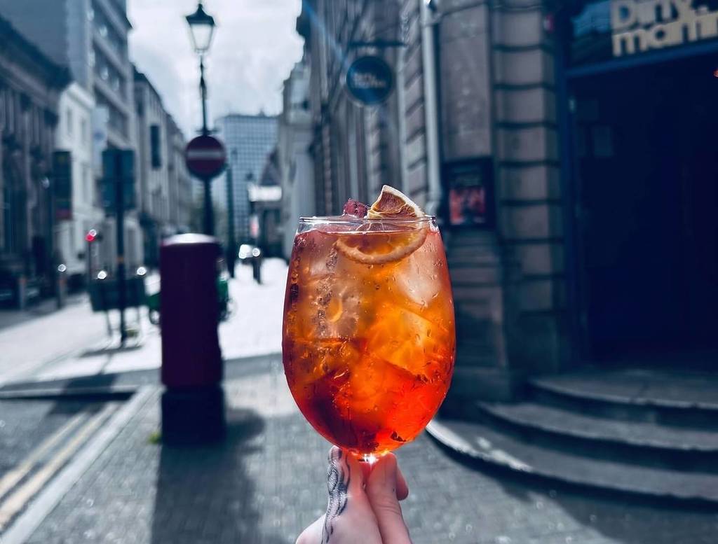 dirty martini aperol spritz held in hand outside the bar