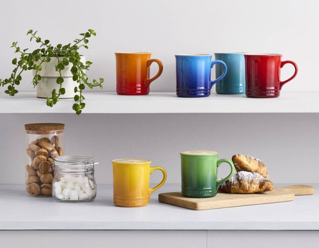 shelving displaying a colourful selection of le creuset mugs, a plant, croissants, and biscuits in a jar