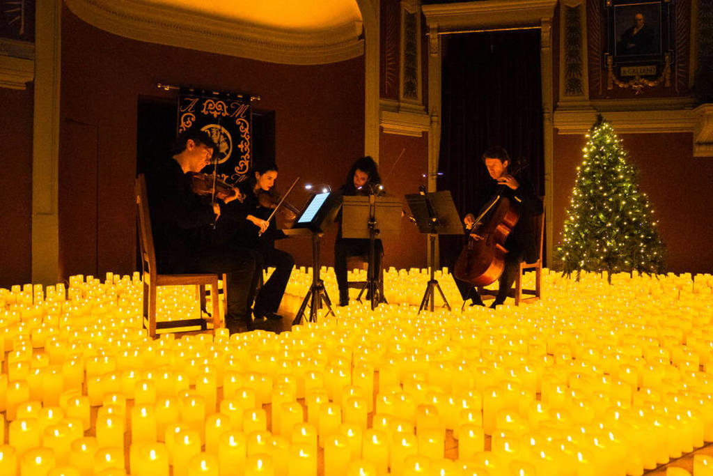 quarteto de cordas tocando em palco iluminado por milhares de velas e a silhueta de duas pessoas sentadas