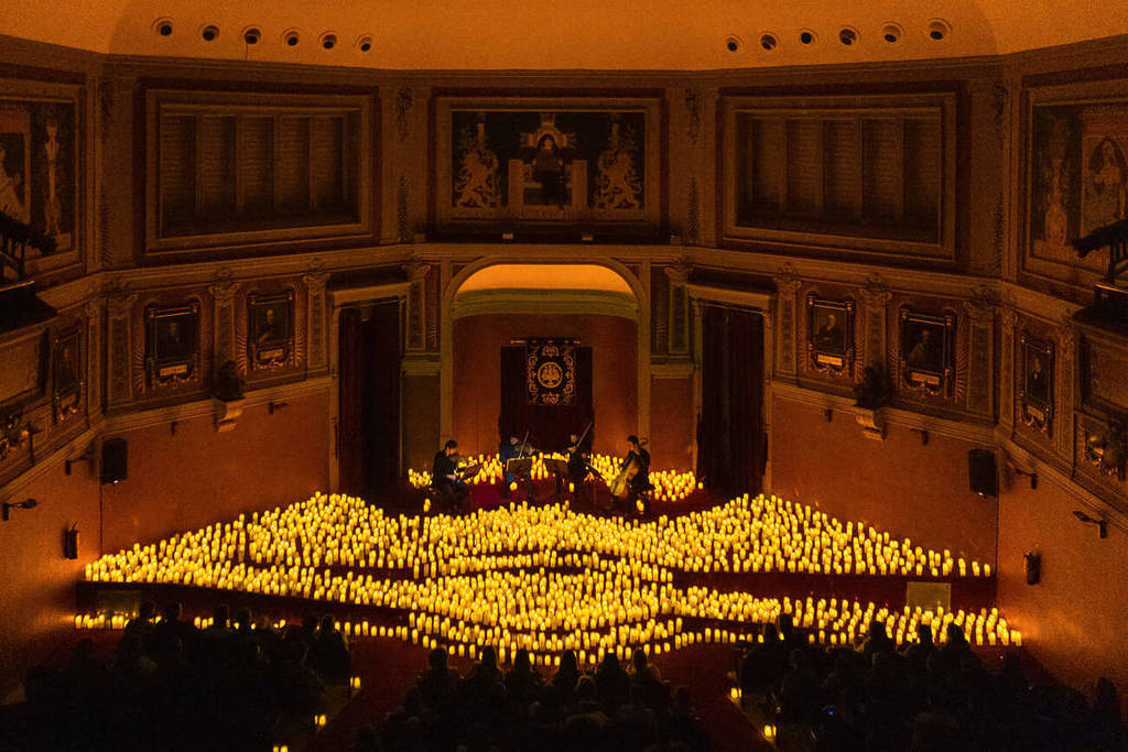 Panoramica di un quartetto d'archi che suona su un palco ricoperto di candele durante un concerto Candlelight all'Ateneo di Madrid.