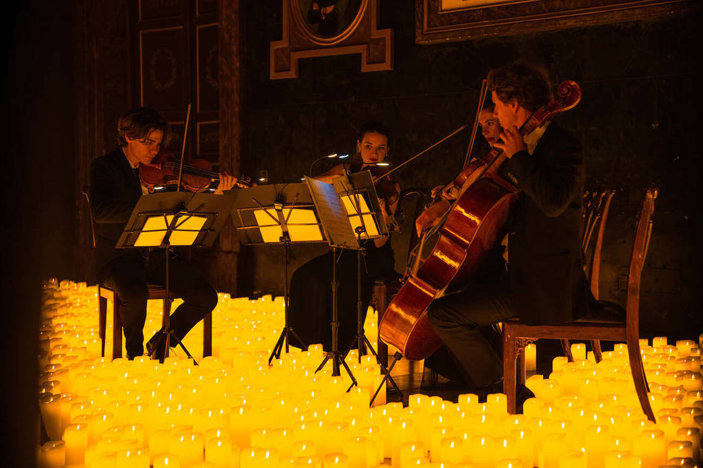 Un cuarteto de cuerda toca sobre un escenario cubierto de velas durante un concierto Candlelight.