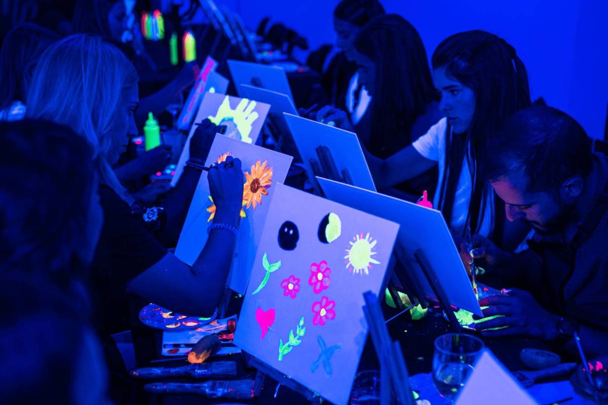 Un grupo de asistentes pinta con pintura fluorescente sobre un lienzo cada uno a oscuras, en Neon Brush.