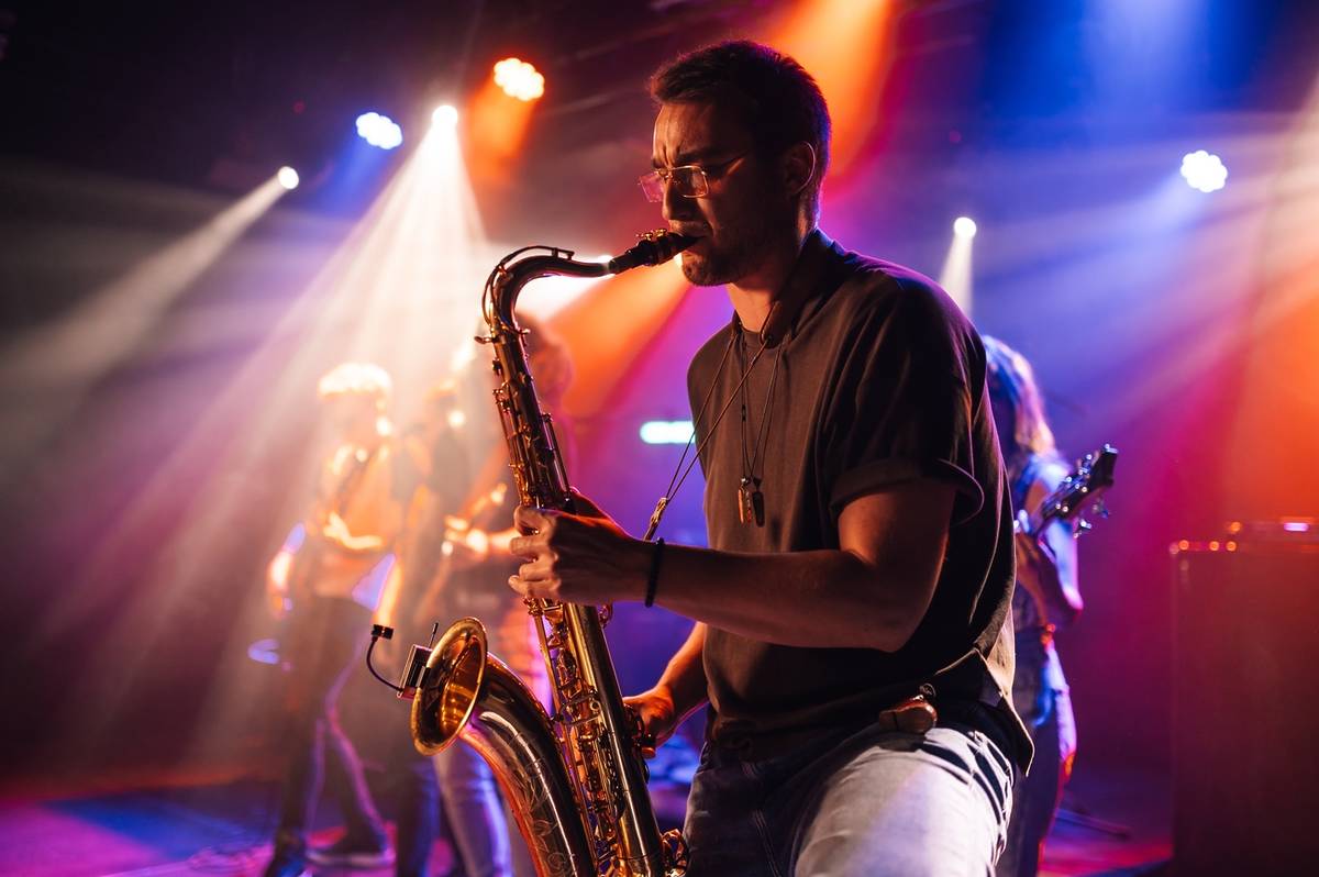 Saxofonista con banda de jazz detrás en un escenario con focos de colores