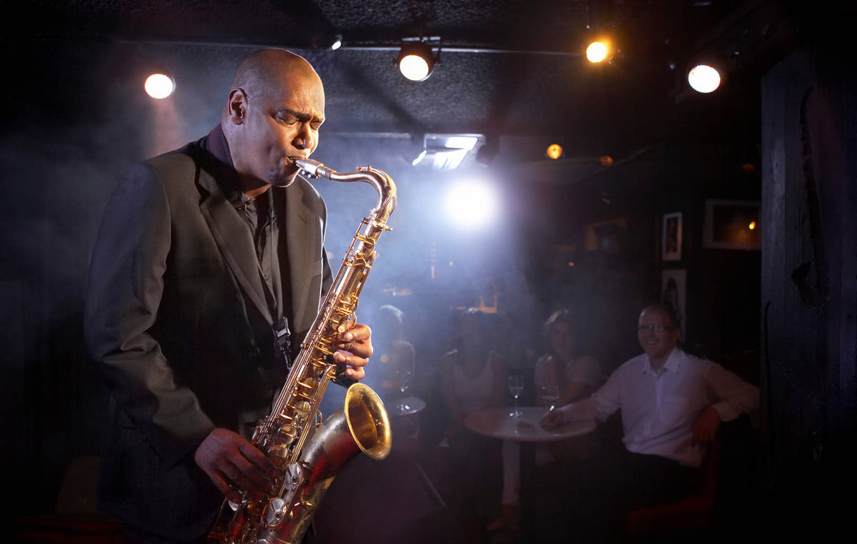 Saxofonista en un escenario de un club de jazz con público en mesas de fondo
