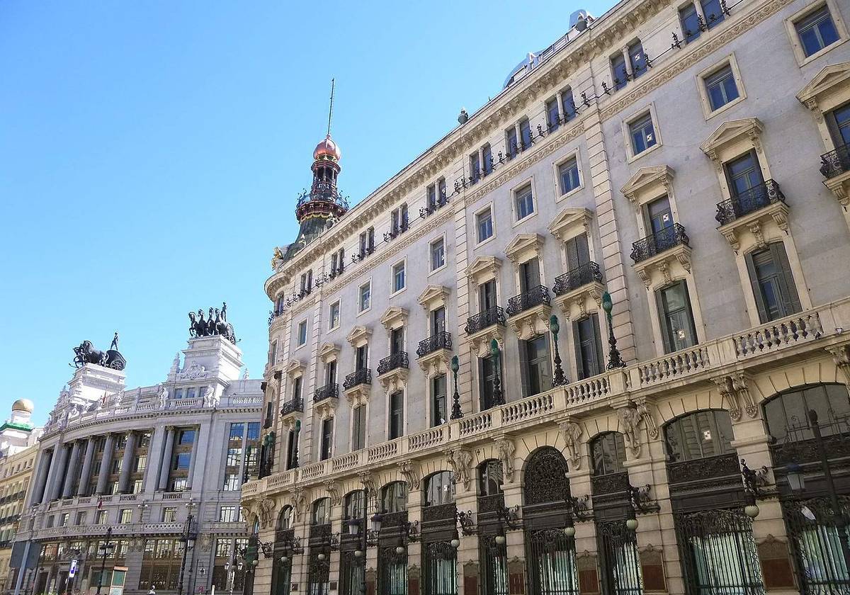 Vista lateral del Four Seasons Hotel Madrid en la calle Alcalá, con balcones de hierro forjado y la cúpula coronando el edificio histórico.