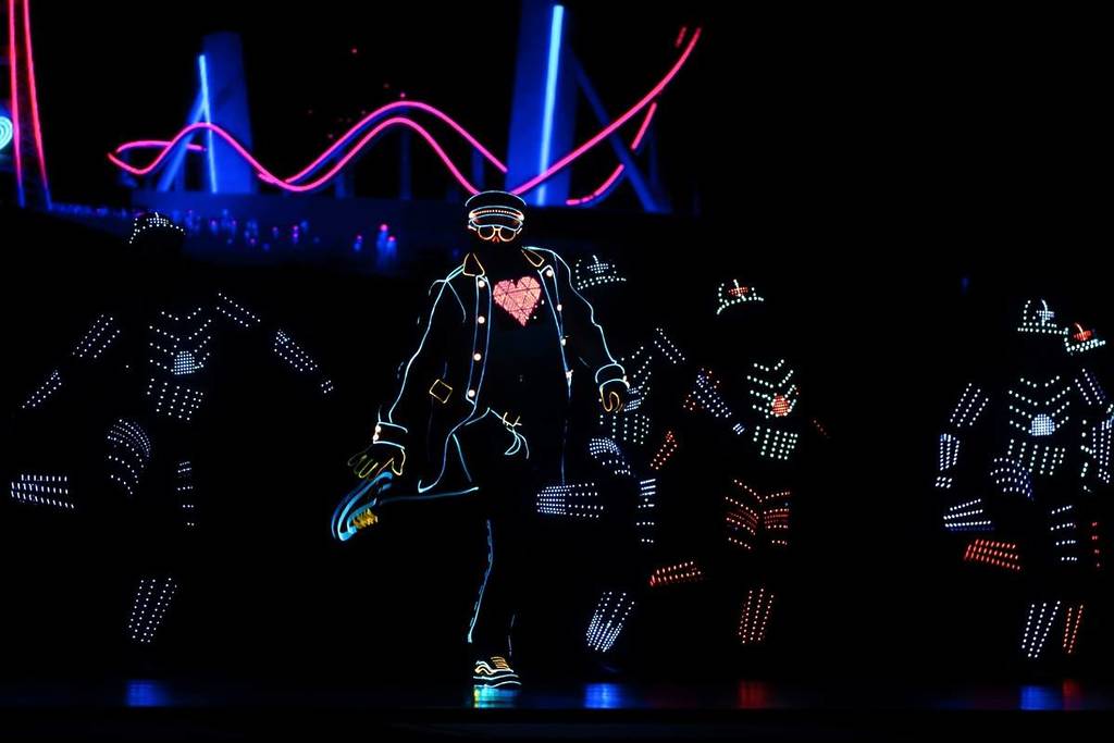 Bailarines con trajes cubiertos de luces LED bailan sobre un escenario a oscuras.