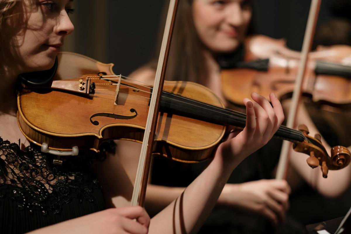 Primer plano de dos violinistas durante un ensayo de una orquesta clásica.