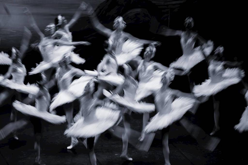 Photo artistique en noir et blanc avec plein de danseuses de ballet dansant en tutu sur une scène.