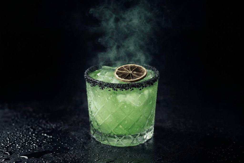 Primer plano de un cocktail verde del que sale humo en Edgar Allan Poe Speakeasy.