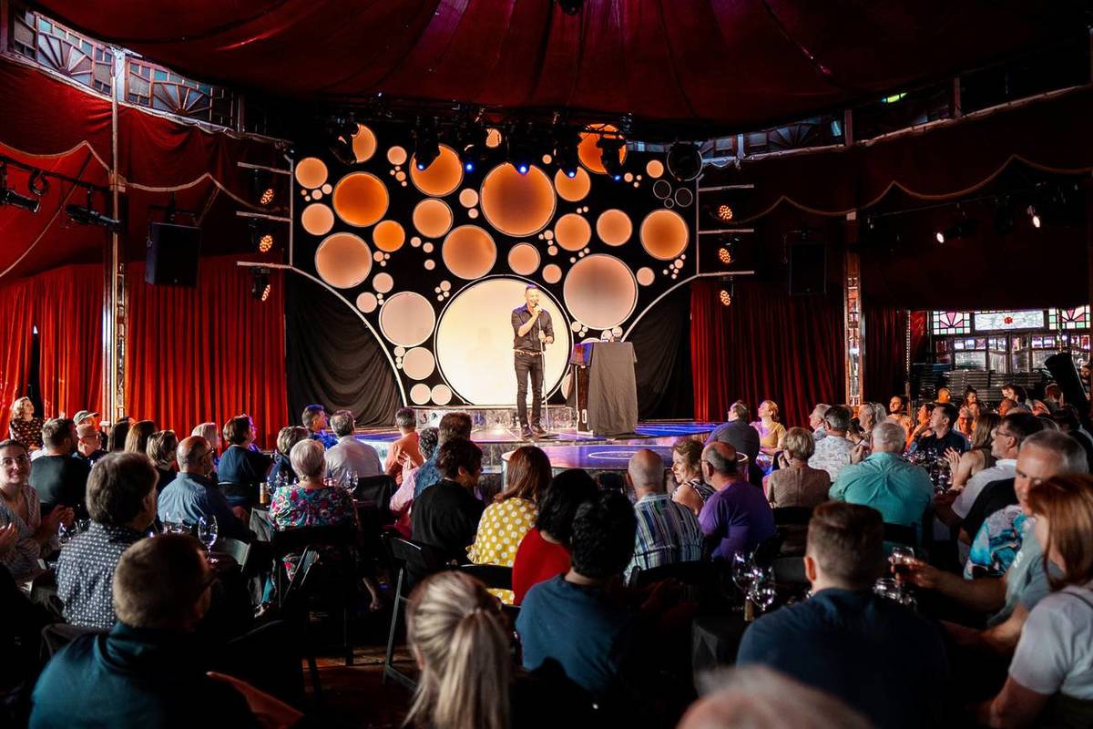 An Idiot's Guide to Wine: eine Comedy-Show, bei der ein Stand-up-Comedian auf der Bühne steht und das Publikum an seinen Tischen sitzt