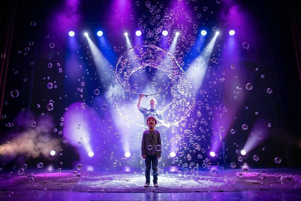 Un niño sobre el escenario mira maravillado la creación de una pompa en BubbleArt Show.