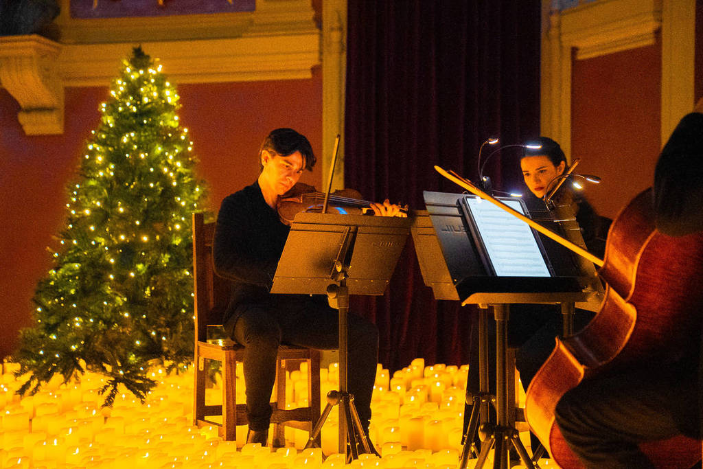 Un cuarteto de cuerda toca sobre un escenario cubierto de velas con un gran árbol de Navidad durante un concierto Candlelight.